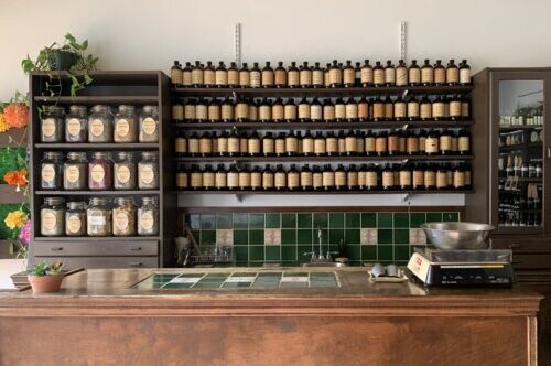 roncy's apothecary & clinic storefront with backwall tincture bottles, and bulk dry loose herb teas on shelves with front wooden counter at forefront with measuring scale