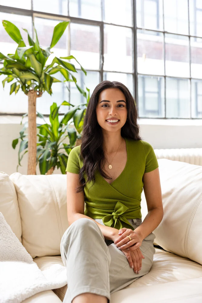 dr arlene dubier headshot naturopathic doctor on white coach with cornplant and windows in the background cropped