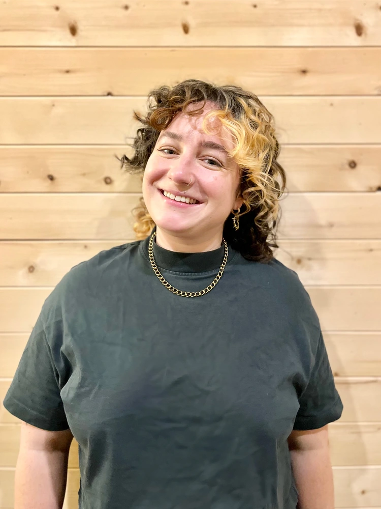 melanie udell acupuncturist headshot against wooden panel wall wearing green shirt at roncys apothecary and clinic