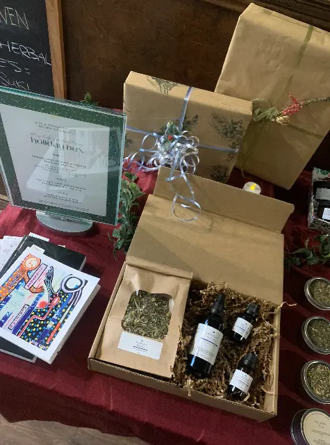 DIY custom holiday kraft box with herbal tea, tincture, and essential oils with wrapped presents in the background on table