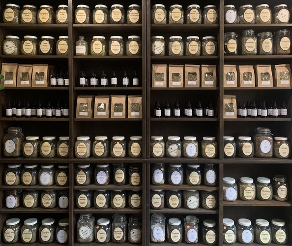 brown shelves with herbal products and glass jars containing dry herbs amber dropper bottles with tinctures and brown paper bags containing herbal tea blends in roncesvalles apothecary and clinic in toronto