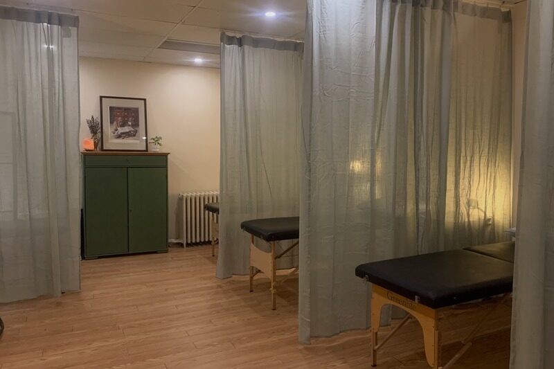 roncesvalles apothecary and clinic community acupuncture room in toronto with sage curtain dividers treatment tables and a green wooden cabinet at the back with decor