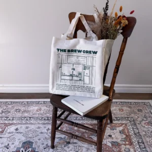 roncys apothecary and clinic canvas tote bag merch with storefront facade on wooden chair dried flowers and lifestyle book